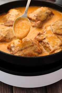 a spoon with some food in it on top of a pan filled with sauce and meat