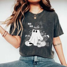 Trendy women's t-shirt with a super cute and creative "BOO BOO" Halloween design. This t-shirt is made from soft and breathable cotton, ensuring absolute comfort while wearing. The standout print features a small ghost wearing a witch hat, surrounded by flowers and two pumpkins, creating a youthful and unique look. * Made with medium fabric (5.3 oz/yd² (180 g/m consisting of 100% cotton for year-round comfort that is sustainable and highly durable. * The classic fit of this shirt ensures a comfy, relaxed wear while the crew neckline adds that neat, timeless look that can blend into any occasion, casual or semi-formal. If you would like to choose a different color for the shirt, please don't hesitate to message the shop. We will assist you if we have that color available. This product is ma Trendy Halloween Short Sleeve T-shirt, Spooky Short Sleeve T-shirt For Fall, Spooky T-shirt With Funny Print In Relaxed Fit, Spooky Cartoon Print T-shirt For Fall, Trendy Halloween Graphic T-shirt, Spooky Relaxed Fit T-shirt With Funny Print, Fall Spooky Cartoon Print T-shirt, Halloween Funny Print Graphic T-shirt, Halloween Graphic Tee With Funny Print