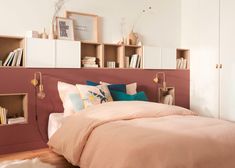 a bed with pink sheets and pillows in a bedroom next to a book shelf filled with books