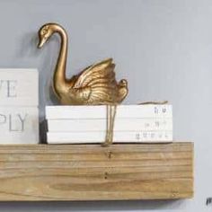 a gold swan figurine sitting on top of a wooden shelf next to books