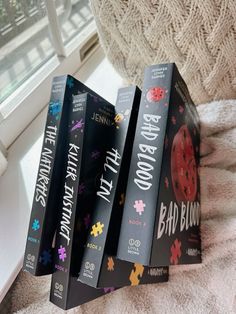 four books sitting on top of a white blanket next to a window sill in a room