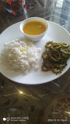 a white plate topped with rice and veggies next to a bowl of soup