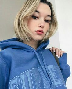 a woman with blonde hair wearing a blue hoodie and looking off to the side