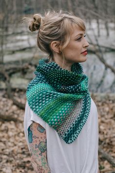 a woman with tattoos wearing a green and white scarf on her neck, standing in the woods