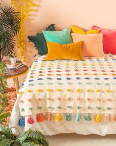 a bed with colorful pillows on top of it and a plant in the corner next to it