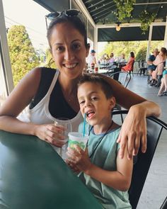 a woman sitting next to a little boy holding a drink in front of her and smiling at the camera