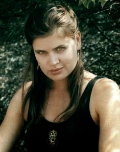 a woman sitting on the ground in front of a tree and looking at the camera