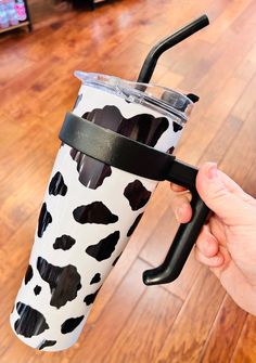 a hand holding a black and white cow print tumbler with a straw in it