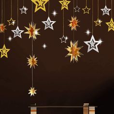 some gold and silver stars hanging from strings on a brown wall in a room with black walls