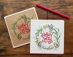 two cross stitch christmas cards on a wooden table