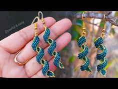 two pairs of gold and blue beaded earrings hanging from a tree branch in front of a hand