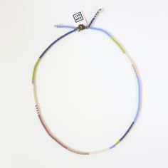 a multicolored beaded necklace on a white surface with a tag attached to it