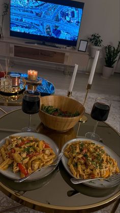 two plates of food on a table in front of a television with candles and wine glasses