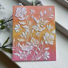 a card with flowers on it sitting next to some white and pink flowers in front of a window