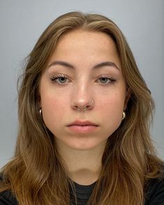 a woman with long hair and piercings looks at the camera while wearing a black shirt