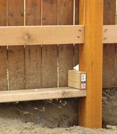 a wooden bench sitting in front of a fence with dirt on the ground underneath it