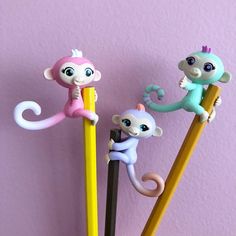 three monkey figurines sitting on top of pencils in front of a pink wall