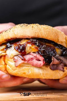 a person holding a sandwich in their hands with meat, cheese and sauce on it