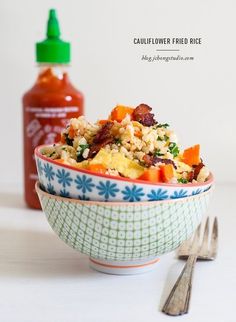 a bowl filled with rice and vegetables next to a bottle of ketchup on the side