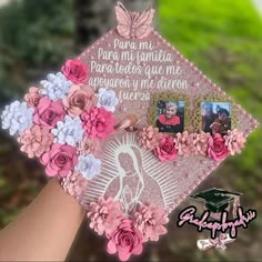 a hand holding a pink and white graduation cap with flowers on the front, decorated with photos