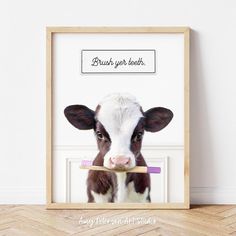 a brown and white cow with a toothbrush in it's mouth, framed in a wooden frame