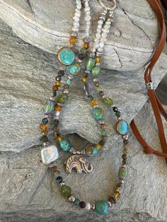 This colorful, double strand, Sundance style beaded necklace is a blend of my favorite colors, blues, yellow, rustic brown and Peridot green. I used tiny freshwater seed Pearls to start it off. Then blended faceted turquoise rounds, Blue and Yellow Chevron beads, a white freshwater Coin Pearl, 4 stunning Kingman Turquoise nuggets, Three natural Peridot nuggets and a ton of Hilltribe Silver!  A Hilltribe Silver Elephant is the focal on the first strand. This hangs from Carmel colored very soft , Bohemian Hand-strung Necklaces For Layering, Bohemian Double Strand Beaded Necklaces With Gemstones, Bohemian Double Strand Gemstone Beaded Necklace, Bohemian Double Strand Gemstone Beaded Necklaces, Bohemian Double Strand Beaded Necklaces With Unique Variations, Bohemian Double Strand Beaded Necklaces, Green Bohemian Double Strand Jewelry, Unique Turquoise Double Strand Necklace, Adjustable Multi-strand Bohemian Turquoise Necklace