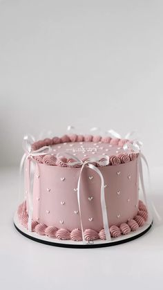 a pink cake with white ribbons and hearts on it