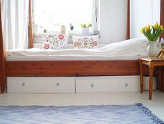 a bed with white sheets and pillows in a room next to a window filled with flowers