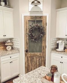 a kitchen with white cabinets and marble counter tops, an old door is open to reveal a wreath