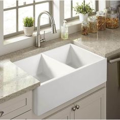 a white kitchen sink sitting on top of a counter next to a potted plant