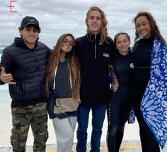 a group of people standing next to each other in front of the ocean on a cloudy day