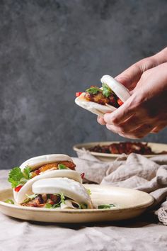 a hand holding a sandwich over a plate with other food on the table behind it