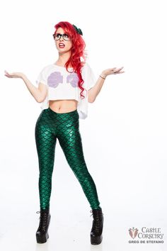 a woman with red hair and glasses is wearing green mermaid leggings while posing for the camera