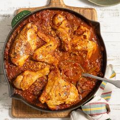 a skillet filled with chicken and sauce on top of a cutting board next to a knife