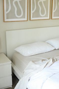 a bed with white sheets and pillows in a bedroom next to two pictures on the wall