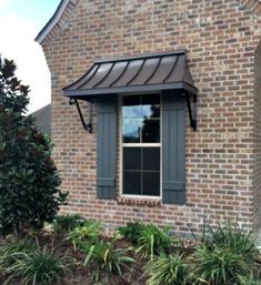 a brick house with a black awning and green plants