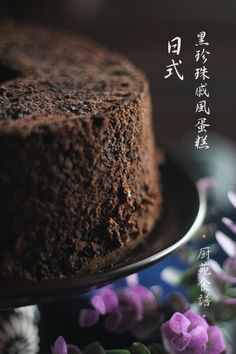 a chocolate cake sitting on top of a plate with purple flowers in front of it