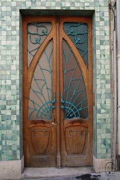 an ornate wooden door with glass panels on the side of a building in front of a green tiled wall