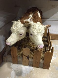 two fake cows sitting on top of a pile of hay in a wooden fenced area