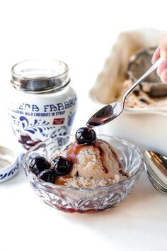 a person scooping ice cream out of a glass bowl with blueberries on top