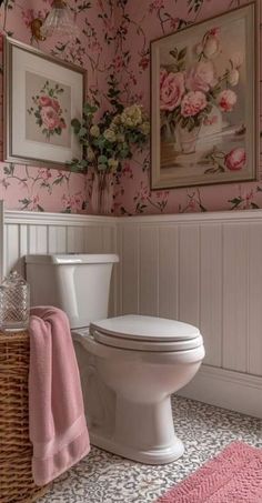 a white toilet sitting in a bathroom next to a pink flower covered wallpaper and framed pictures