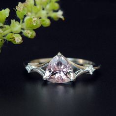 a pink diamond ring sitting on top of a table next to a flower pot with flowers in it