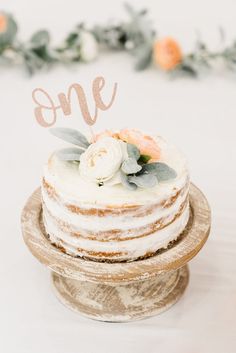 there is a cake with flowers on the top and one sign above it that says, one