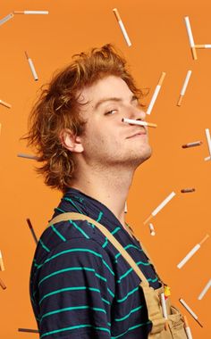 a man standing in front of an orange background with matches sticking out of his mouth