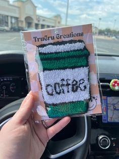 someone is holding up a crocheted coffee cup in their car dashboard with the word starbucks written on it