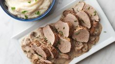 some meat and mashed potatoes on a white plate with gravy next to it