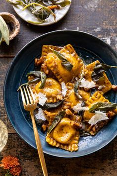 a blue plate topped with ravioli covered in sauce and cheese next to a fork