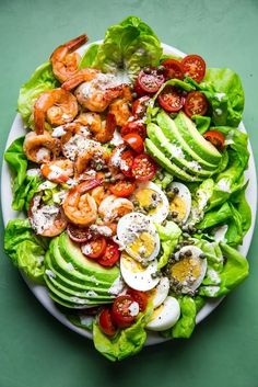 a salad with shrimp, avocado and tomatoes on it is shown in a white plate