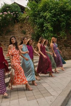 a group of women walking down a sidewalk next to each other in dresses and sandals