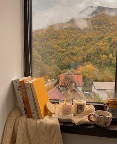 a window sill with books and cups on it in front of a mountain view